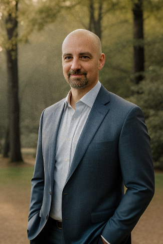 Curtis Jones, Orlando wedding photographer, in a suit stands outdoors at Orlando wedding venue The Veranda at Thornton Park, with hands in pockets and a slight smile. Trees and a natural setting are visible in the background.