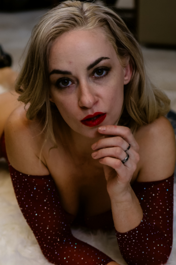 A woman with blonde hair and red lipstick lies on her stomach, wearing an off-the-shoulder top with sparkles.